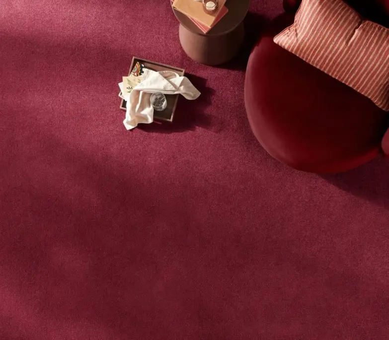 A photograph looking down on a scarlet red carpet with a red chair and pink cushion.
